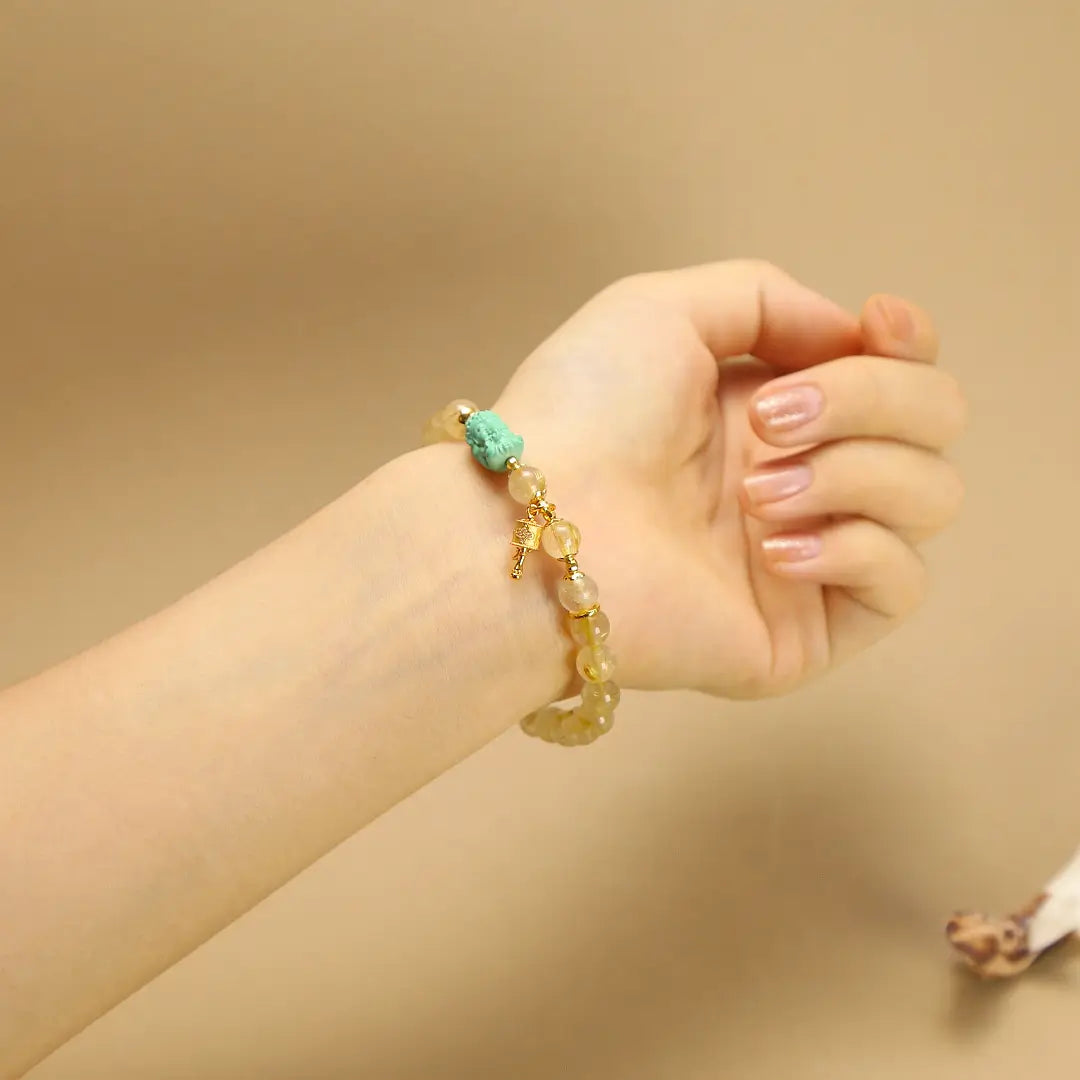 Woman wearing a Golden Rutilated Quartz Bracelet on wrist, showing the Green Agate Ganesha, Prayer Wheel and 7mm bead size.